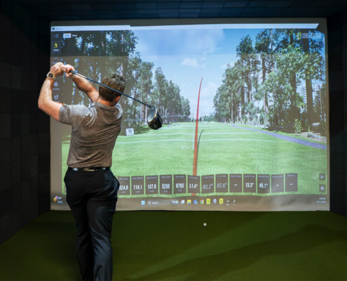 Man practicing drives in a golf simulator receiving golf coaching