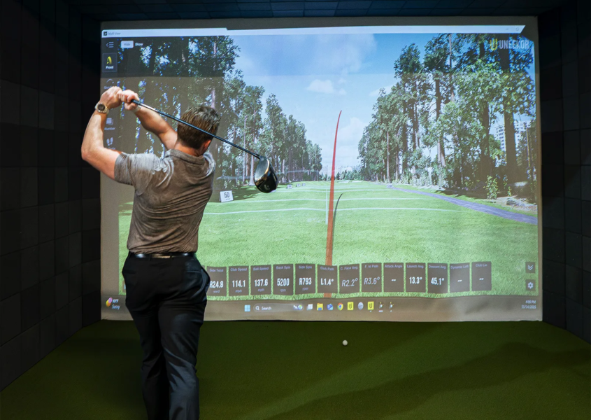 Man practicing drives in a golf simulator receiving golf coaching