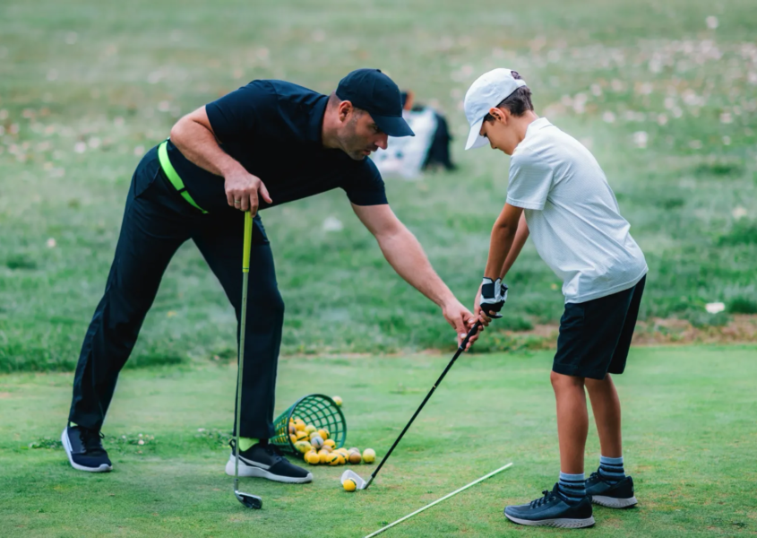 Golf instructor teaching grip and posture to child during junior golf lessons